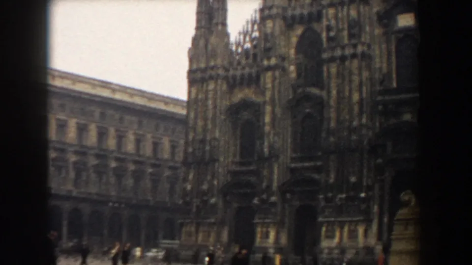 The camera shifts lower on Milan Cathedral, with the piazza edge, nearby building, and distant pedestrians visible in the 1959 view.