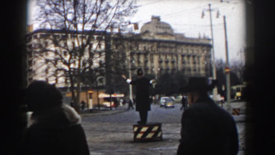 Pisa, Italy in 1959, with a traffic officer using hand signals beside a striped barrier as classic cars move through the street.