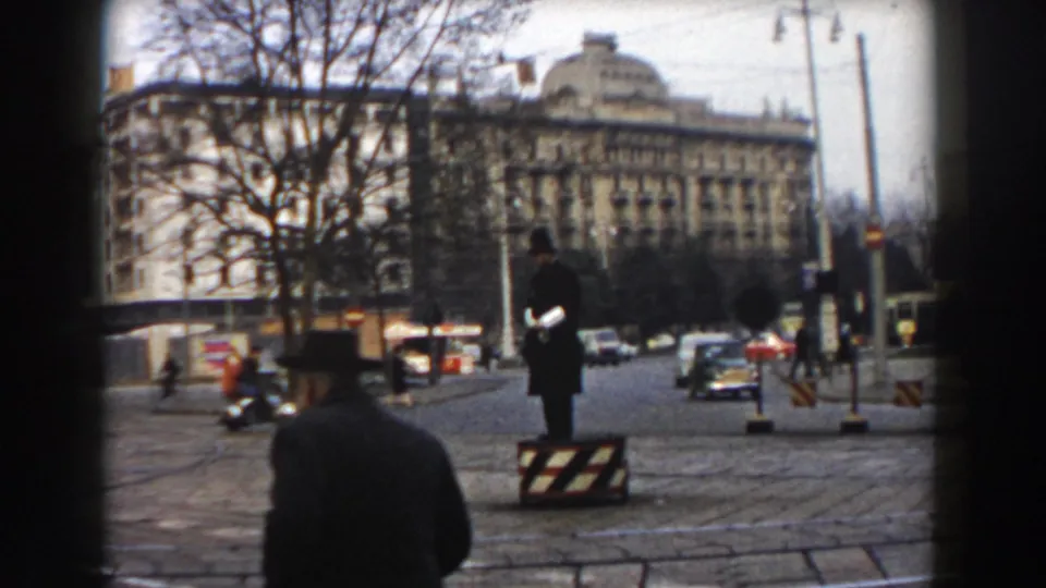 Pisa, Italy street scene from 1959 showing a uniformed traffic officer, street barriers, passing cars, pedestrians, bare trees, and a prominent building.