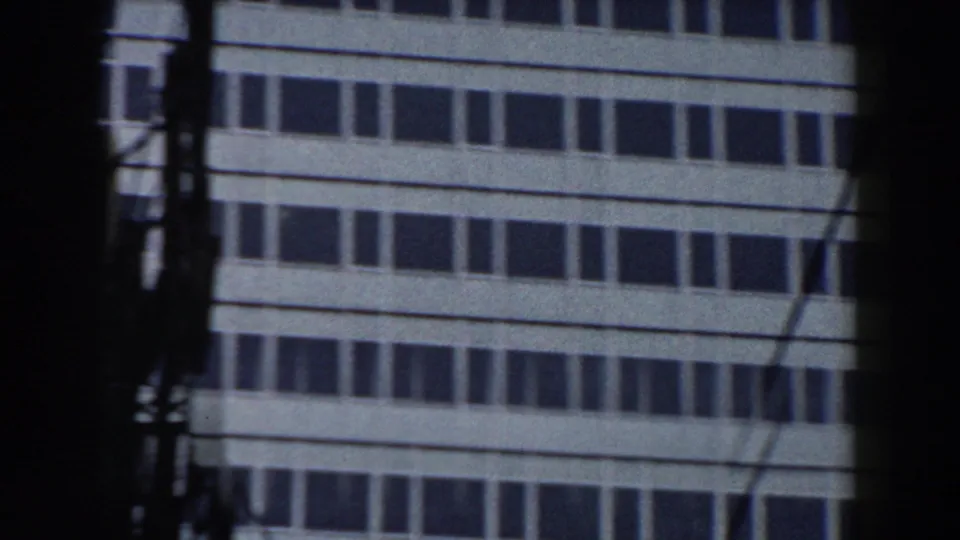 1959 Pisa home-movie frame showing lower rows of a windowed building partly obscured by poles, wires, and dark frame edges.