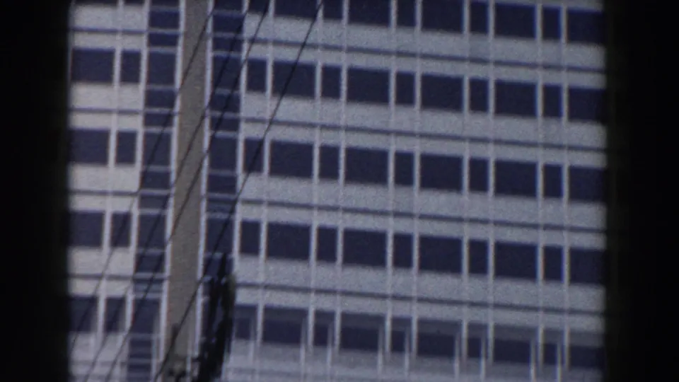 1959 Pisa frame showing a modern facade with a central vertical structural element, window rows, and utility wires in front.