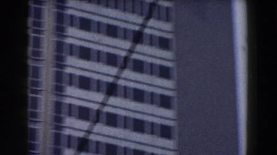1959 Pisa 8mm frame of a modern high-rise facade, with horizontal window rows and a dark vertical element blocking the center.