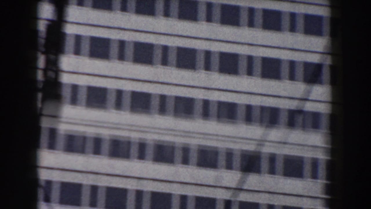 High-rise building facade seen through a dark window frame with wires crossing the view.