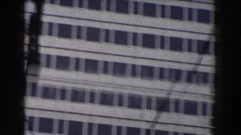 1959 Pisa home-movie frame showing a modern building facade through a dark window edge, with overhead wires cutting across the windows.
