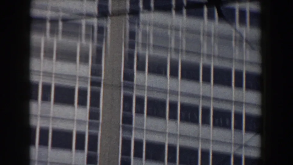 1959 Pisa frame with vertical window lines on a modern building, partly bordered by a dark interior window frame and crossed by faint wires.