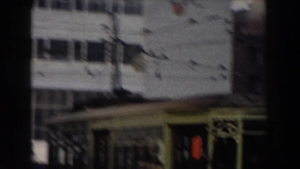 1959 Pisa frame showing a building facade behind crossing wires and dark foreground framing, with a lower roofline or street structure at the bottom.