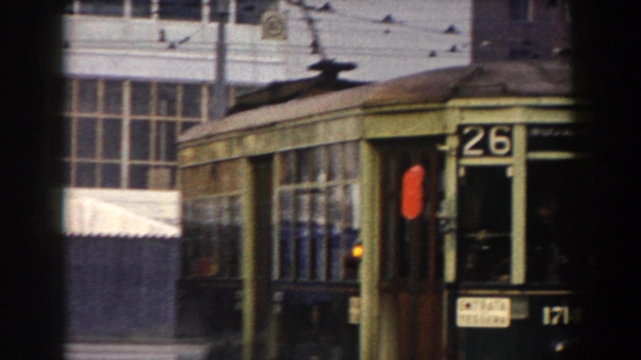 Green tram marked 26 passing on a city street with large windows behind it.