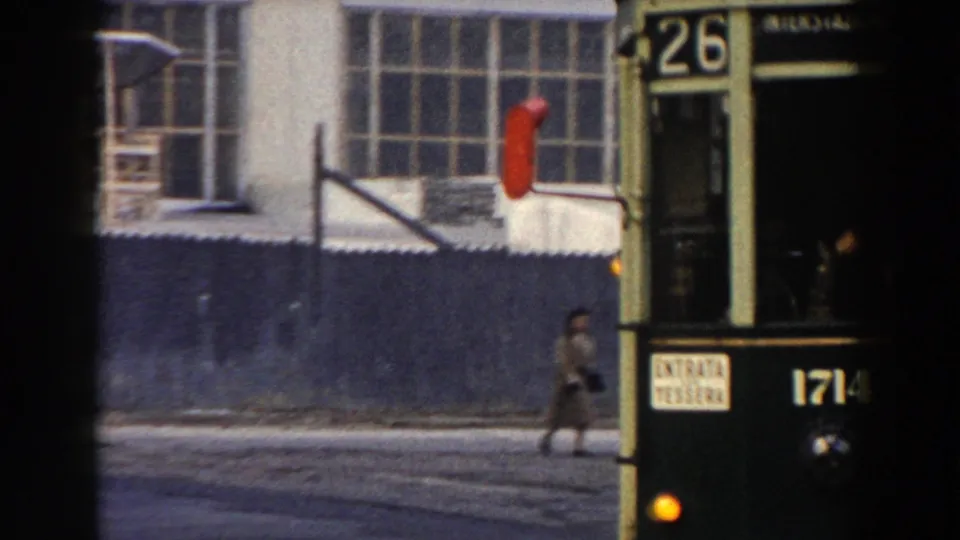 1959 Pisa street view with the front of a tram marked 26 at right and a pedestrian crossing near industrial-style windows.