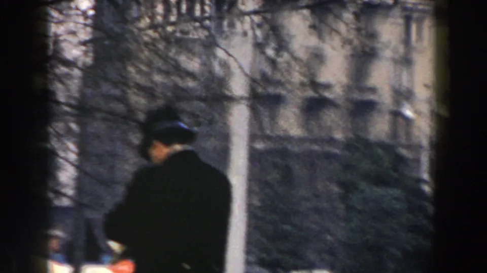 1959 Pisa street frame with a man in a dark coat and hat in front of trees and historic-looking architecture.