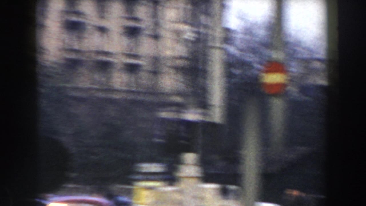 Blurred street view with stone buildings, bare trees, a pole, and a red and yellow traffic sign.