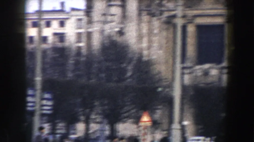 Soft 8mm view of Pisa street architecture, bare trees, parked cars, and a triangular traffic sign at the right edge.