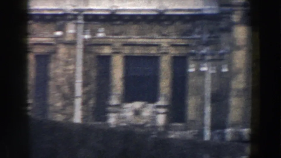 1959 Pisa street-level facade with stonework, columns, poles, and a dark opening captured from a moving 8mm camera.