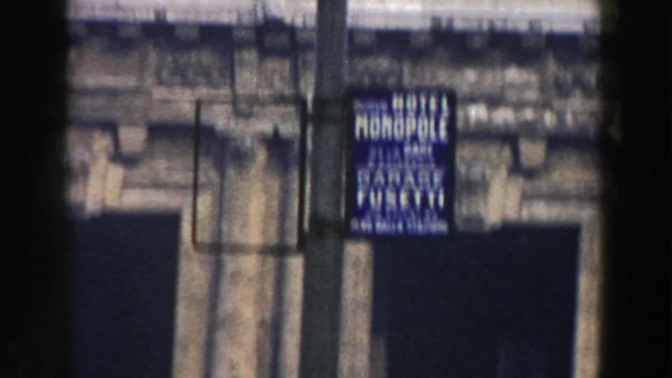 Blue hotel garage sign, possibly reading Hotel Monopoly Garage, seen beside a pole against a stone facade in Pisa.