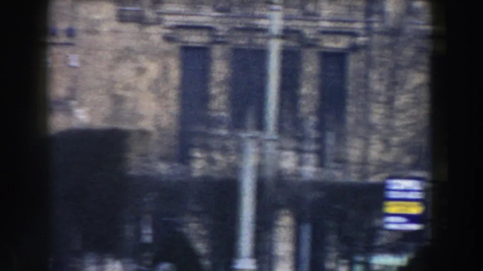 1959 Pisa home-movie frame showing a street-level building facade with windows, a lamp post, signs, and heavy foreground shadow.