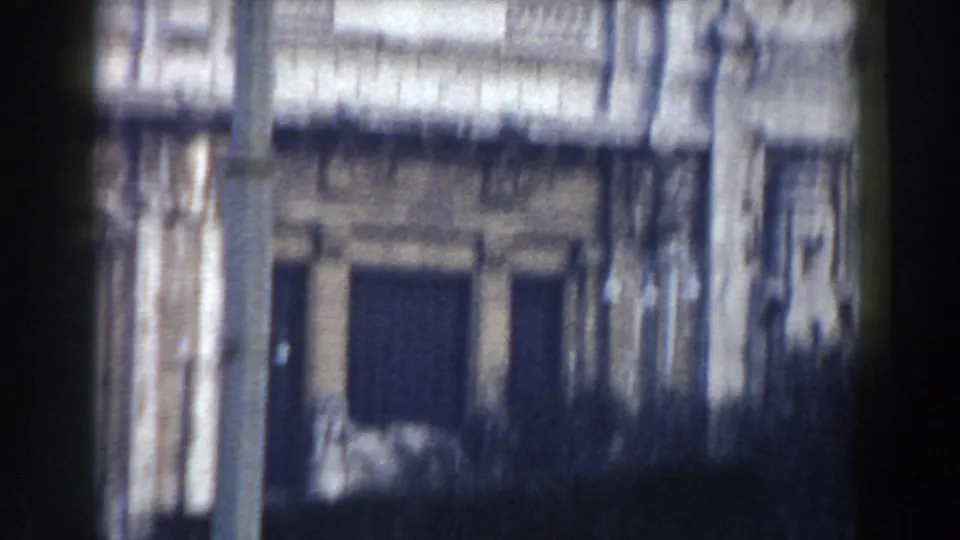 1959 Pisa frame showing a pale historic facade with a dark doorway, architectural trim, and shadow from the moving viewpoint.