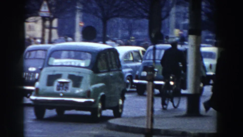 Pisa street view with mid-century cars, a cyclist, bare trees, and pedestrians in a soft 8mm frame.