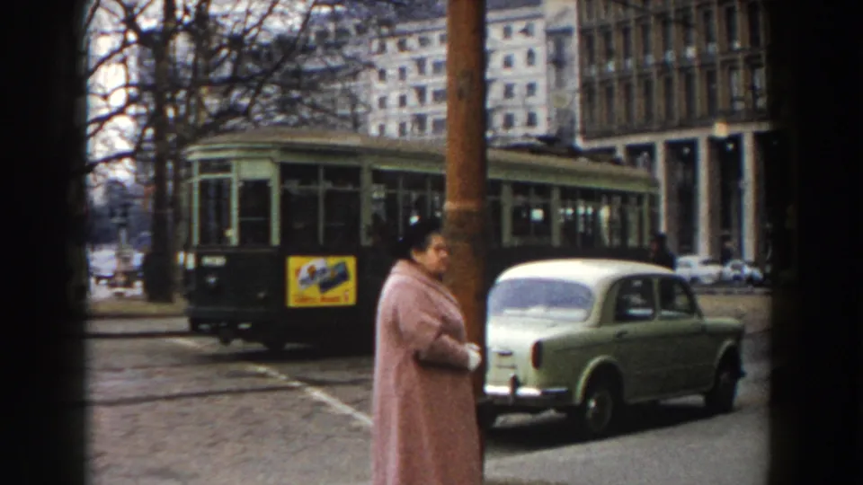 The final frame shows the woman in profile on the Pisa street, with a pale compact car, green tram, leafless trees, and mid-century buildings in view.
