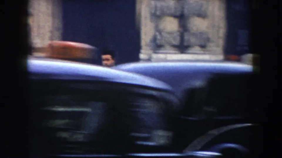 A vintage car crosses the foreground in Pisa, with a partially visible man and large stone architectural details behind it.