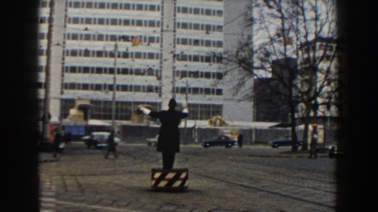 Traffic director on a raised platform in a city street with cars, tram tracks, and a large white building.