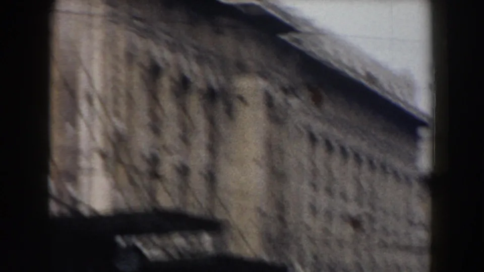 Soft, moving 8mm view of a Pisa masonry facade with a sloped roofline and dark foreground edge crossing the lower frame.