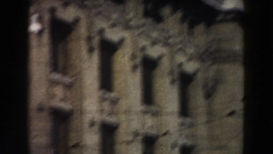 1959 Pisa 8mm frame showing a blurred historic stone facade with tall narrow windows and a tree partially obscuring the view.