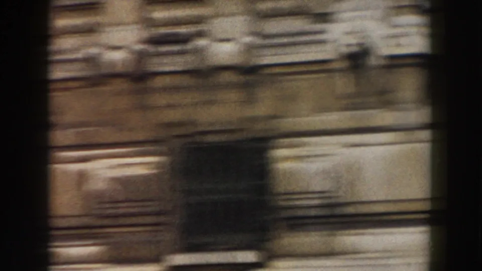 1959 Pisa travel frame with a motion-smeared building facade, balcony or railing lines, and dark vertical obstructions from the moving camera.