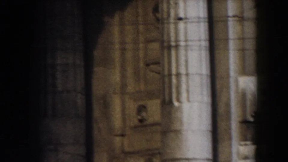 1959 Pisa 8mm frame showing pale stone columns and carved wall sections, partly blocked by dark foreground shapes and soft focus.