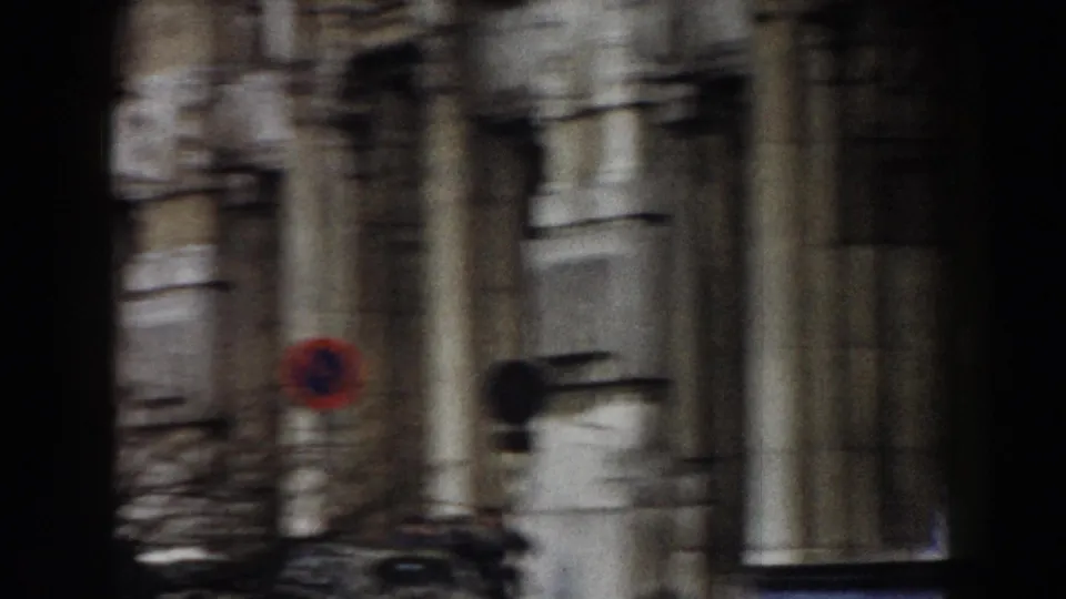 1959 Pisa home-movie frame with motion blur across stone architecture and a circular roadside sign at street level.