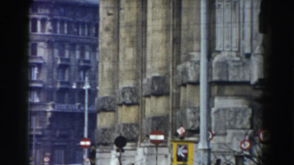 1959 8mm footage identified as Pisa, Italy, showing a weathered stone architectural facade with street signs and a city building beyond it.