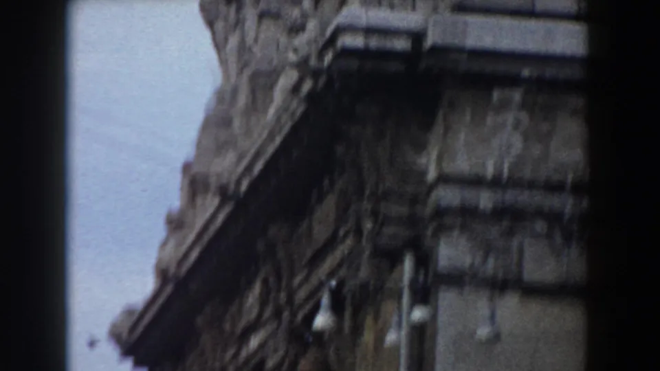 Handheld 8mm view of ornate stone building detail, with a dark vertical film edge dividing the frame and pale sky between structures.