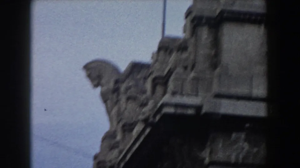 1959 Pisa home-movie frame showing a dark stone sculptural figure or gargoyle-like detail near a pale building edge.