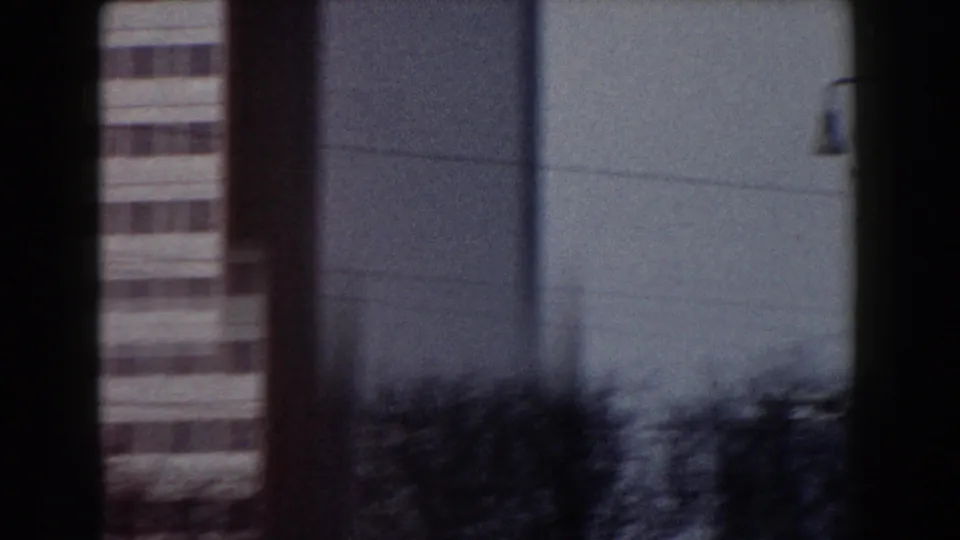 1959 Pisa home-movie view of pale modern architecture with a narrow striped facade and dark foreground dividers.