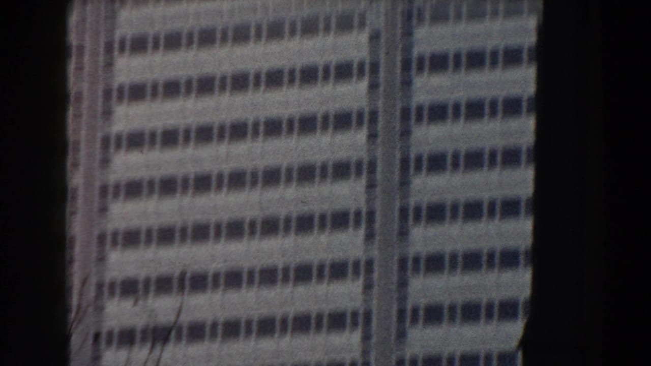 Soft handheld view of a gridded high-rise facade framed by dark vertical edges.