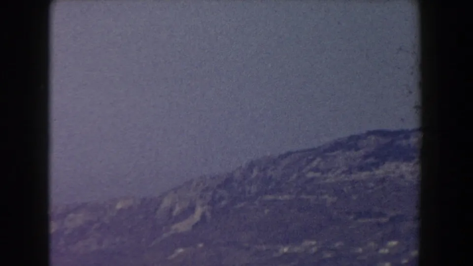 1959 Pisa travel frame shifts from architecture to a grainy distant hillside beneath a muted sky.