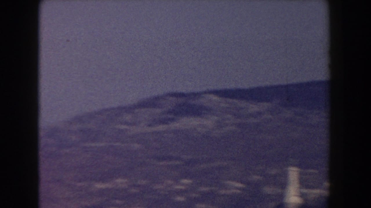 Distant city buildings below rolling hills under a hazy sky.