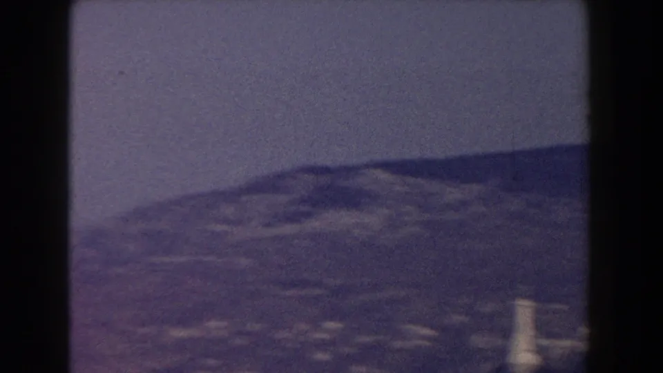 1959 8mm home-movie frame showing a soft aerial view over Pisa, with distant buildings and hills under a hazy sky.