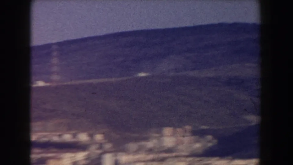 1959 8mm frame from Pisa showing a hillside landscape with scattered buildings and a muted, purple-shifted film palette.