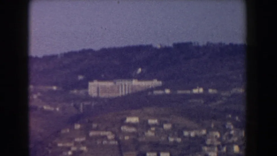 1959 Pisa, Italy 8mm frame showing a hazy hillside town and a large pale building seen from a distance.