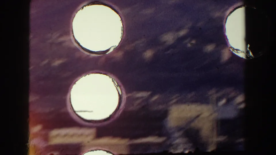 1959 Pisa, Italy 8mm frame showing exposed sprocket holes and film edge over a blurred waterfront and docked boat area.