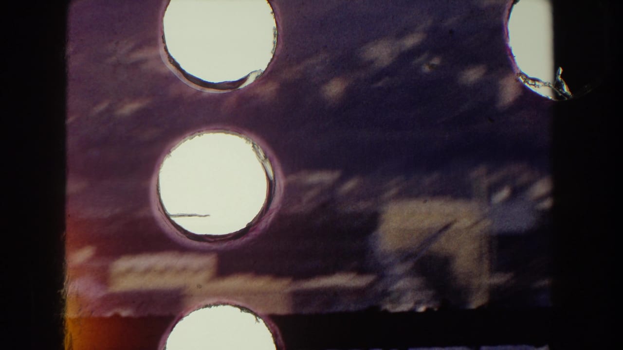 Close-up of 8mm film with bright circular perforations and purple-red light leaks.
