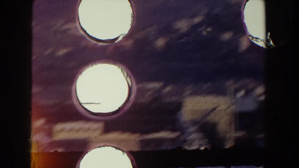1959 8mm home-movie frame detail from the Pisa reel showing sprocket holes, dark dividers, and faded purple-red exposure marks.