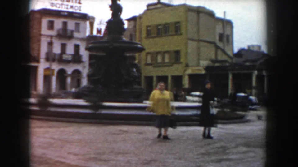 The final frame shows the women in the Pisa square with the fountain between them and a visible hotel sign on a building behind.