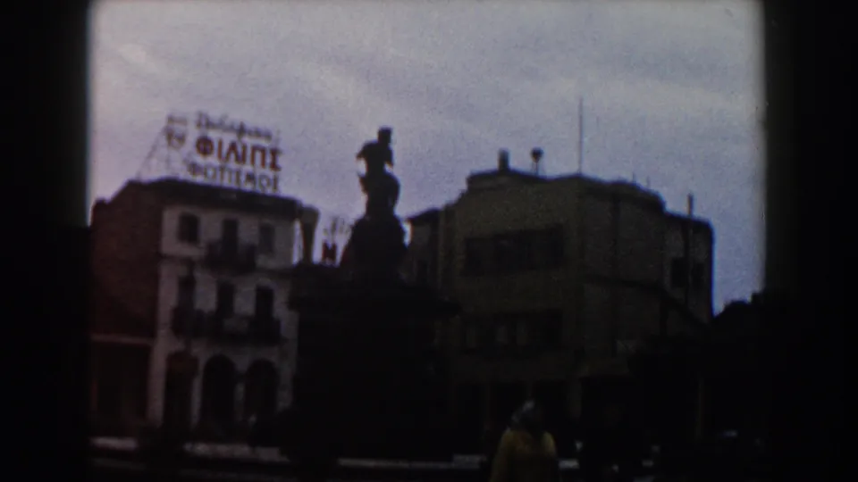 Dark 1959 Pisa frame showing the fountain and square buildings in silhouette, with a rooftop sign and a partly visible pedestrian near the lower edge.