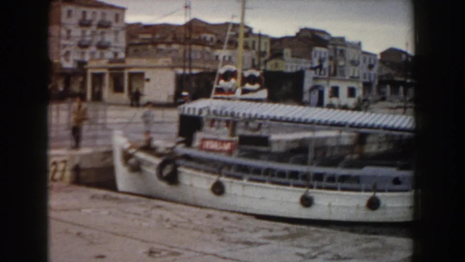 A dockside view shows the ITALIA ferry moored at a harbor quay, with people near the vessel and older waterfront buildings beyond.