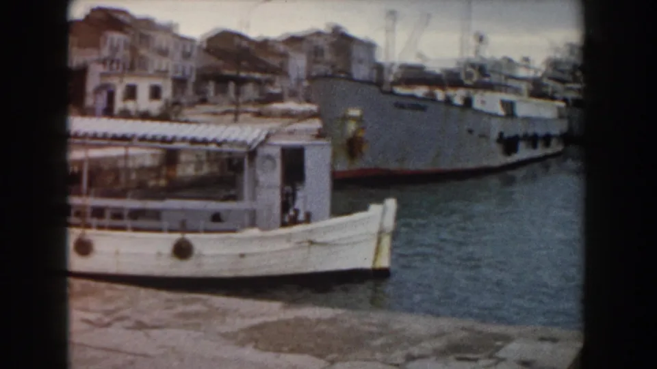 A white passenger ferry sits close to the pier while a larger gray ship appears in the Pisa harbor background.