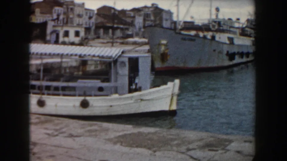 The small white ferry is framed against a larger ship and waterfront buildings in this 1959 Pisa harbor view.