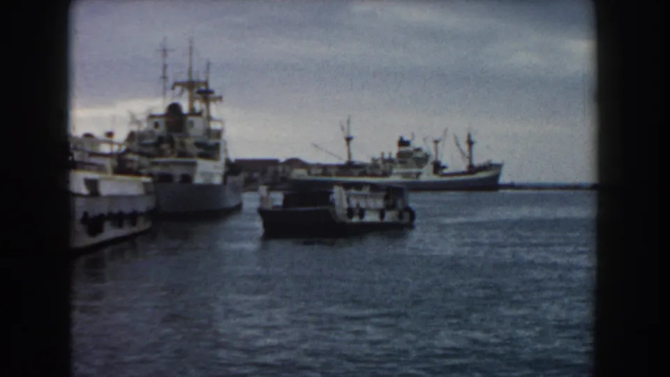 1959 Pisa coastal harbor footage showing moored ships at left and a smaller vessel on the water near the shoreline.