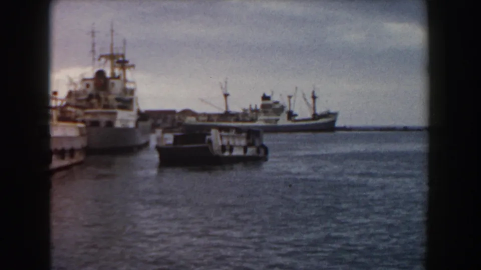 1959 Pisa harbor frame with large vessels to the left, a small boat in front, and rippled water filling the foreground.