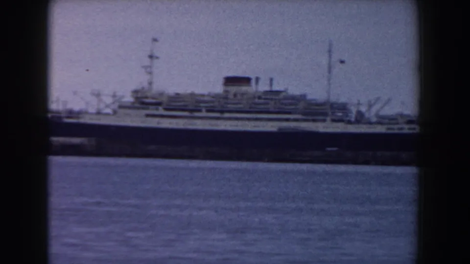 A side view of the large liner fills more of the frame, showing layered white decks, rigging and a dark hull at the dock.