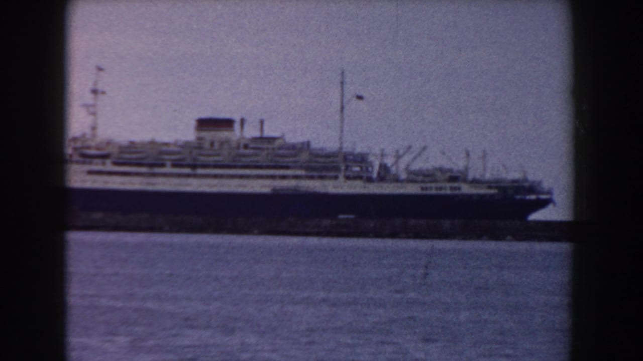 Large passenger ship seen across harbor water through dark frame divisions.